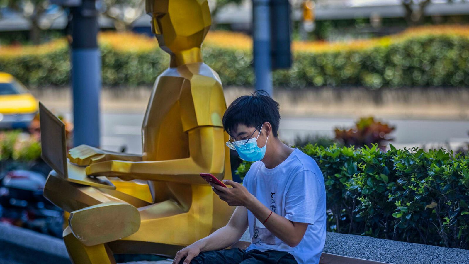 Un hombre usa su teléfono junto a una escultura en Shanghai, China. 