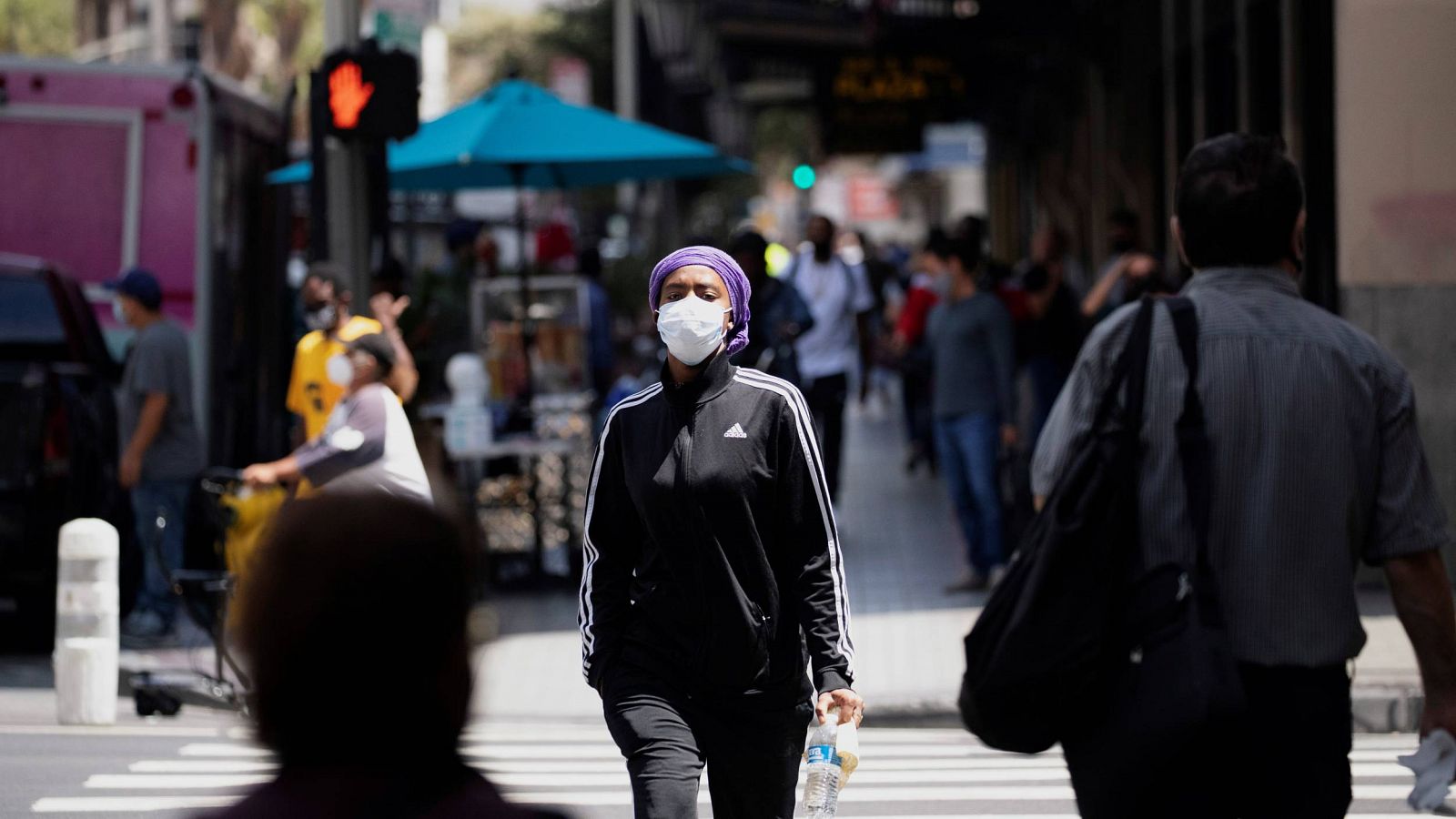 Una mujer con mascarilla cruza una calle en Los Ángeles