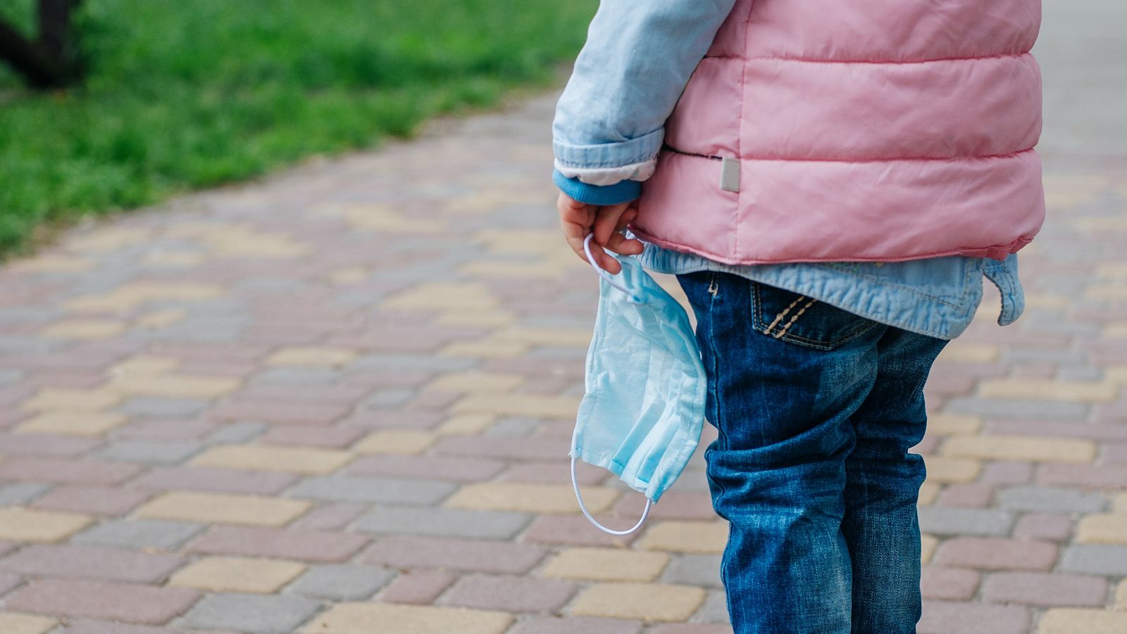 Una niña sostiene una mascarilla mientras camina por la calle.