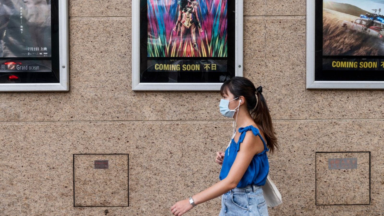 Una mujer con mascarilla pasa por delante de un cine en Hong Kong