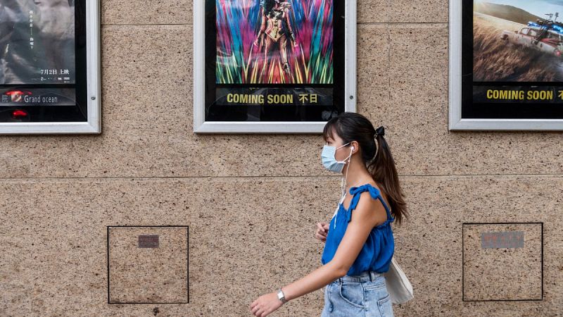 Una mujer con mascarilla pasa por delante de un cine en Hong Kong