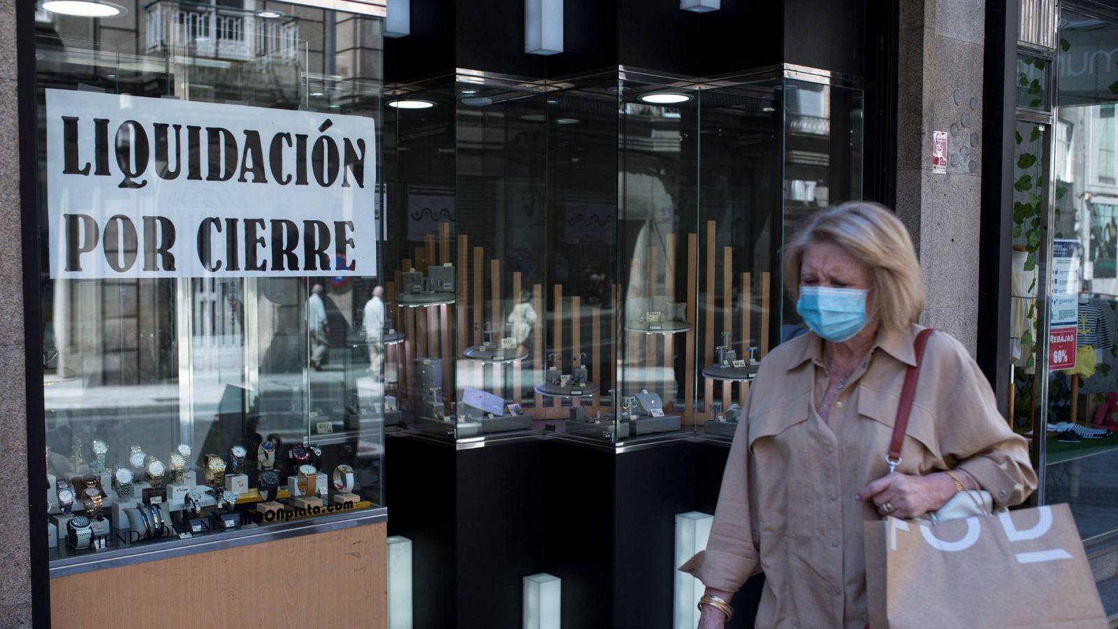 Una mujer con mascarilla pasa ante un comercio con un cartel de "liquidación por cierre" en Ourense