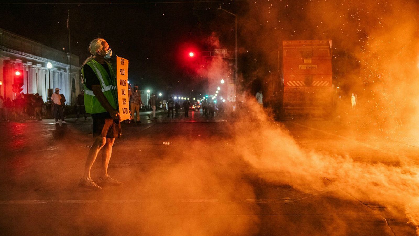 Un hombre está parado con un cartel en Kenosha, Wisconsin en la segunda noche de disturbios después del tiroteo de Jacob Blake. 