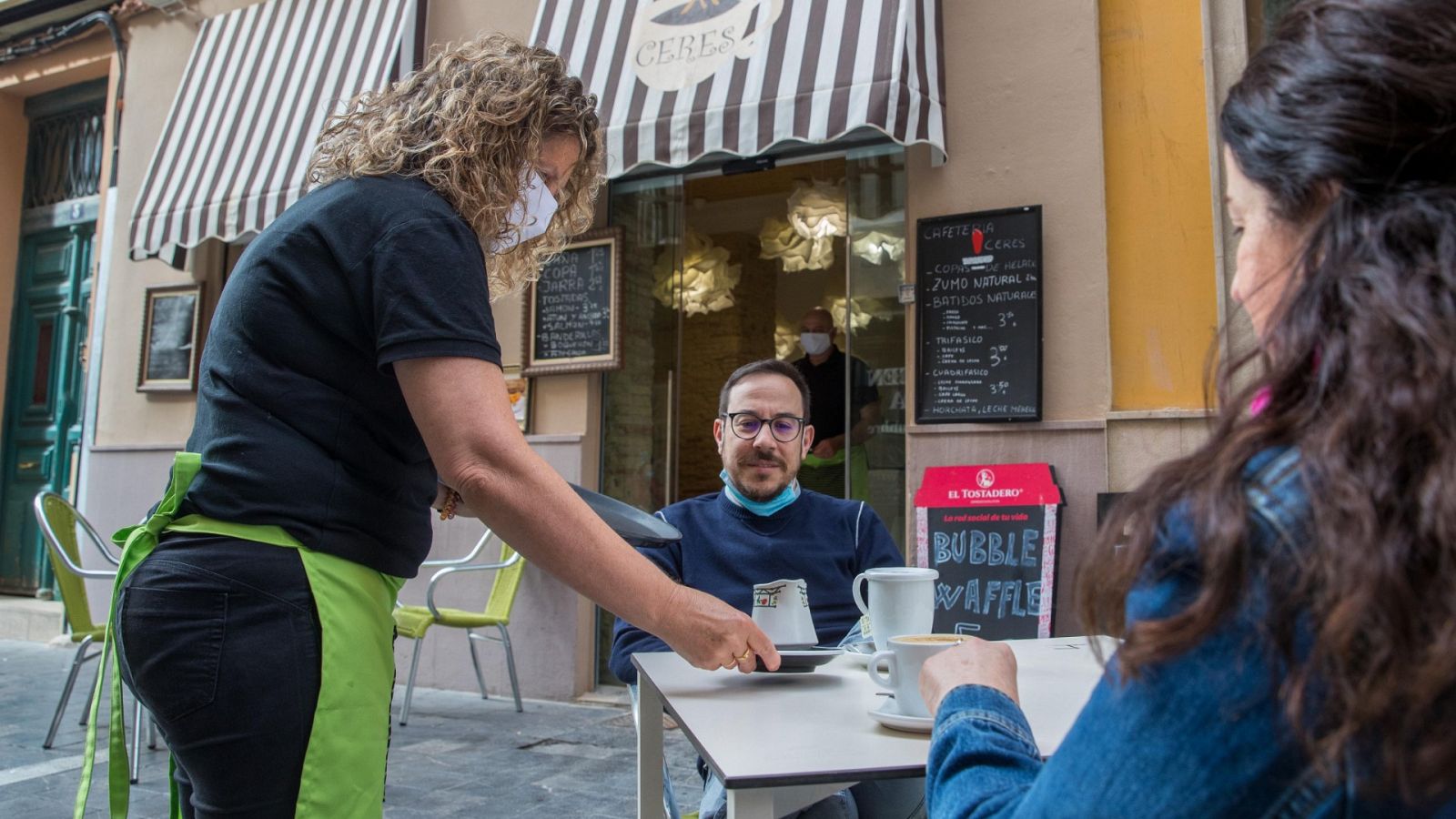 Una camarera atiende a una pareja en la terraza de una cafetería en Zaragoza