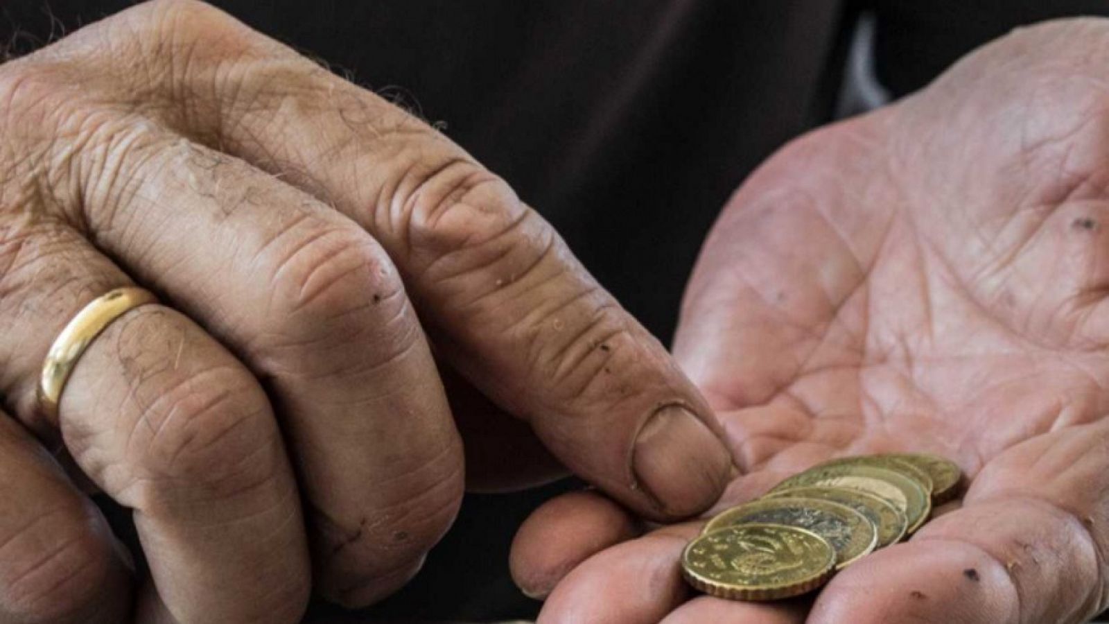 Imagen de las manos de un hombre mayor sujetando varias monedas. 