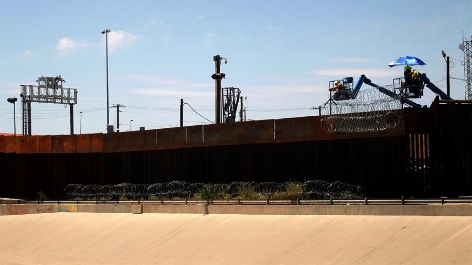 Un grupo de trabajadores contratados por una empresa de autoridades migratorias de EUA, refuerza la seguridad en el muro construido en la frontera, con espirales de alambre de púas hoy martes, para evitar el cruce de migrantes.