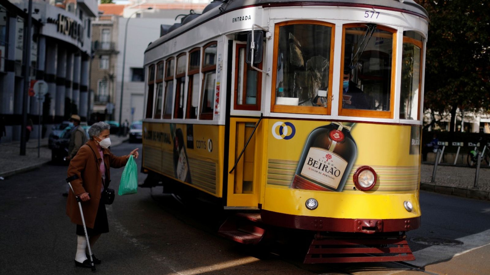 Un señora mayor usando mascarilla dirigiéndose hacia un tranvía en Lisboa, Portugal.