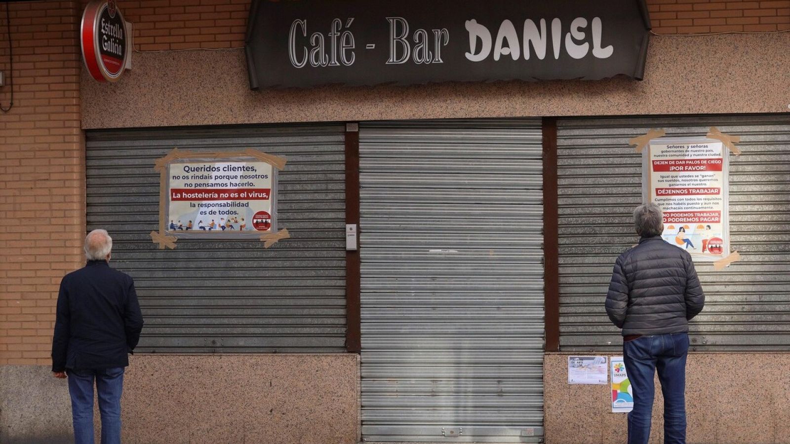 Vecinos leen los carteles de protesta colocados por un hostelero a las puertas de su negocio cerrado en Salamanca, este domingo, durante el primer fin de semana que permanece cerrada en Castilla y León. EFE/ JM Garcia