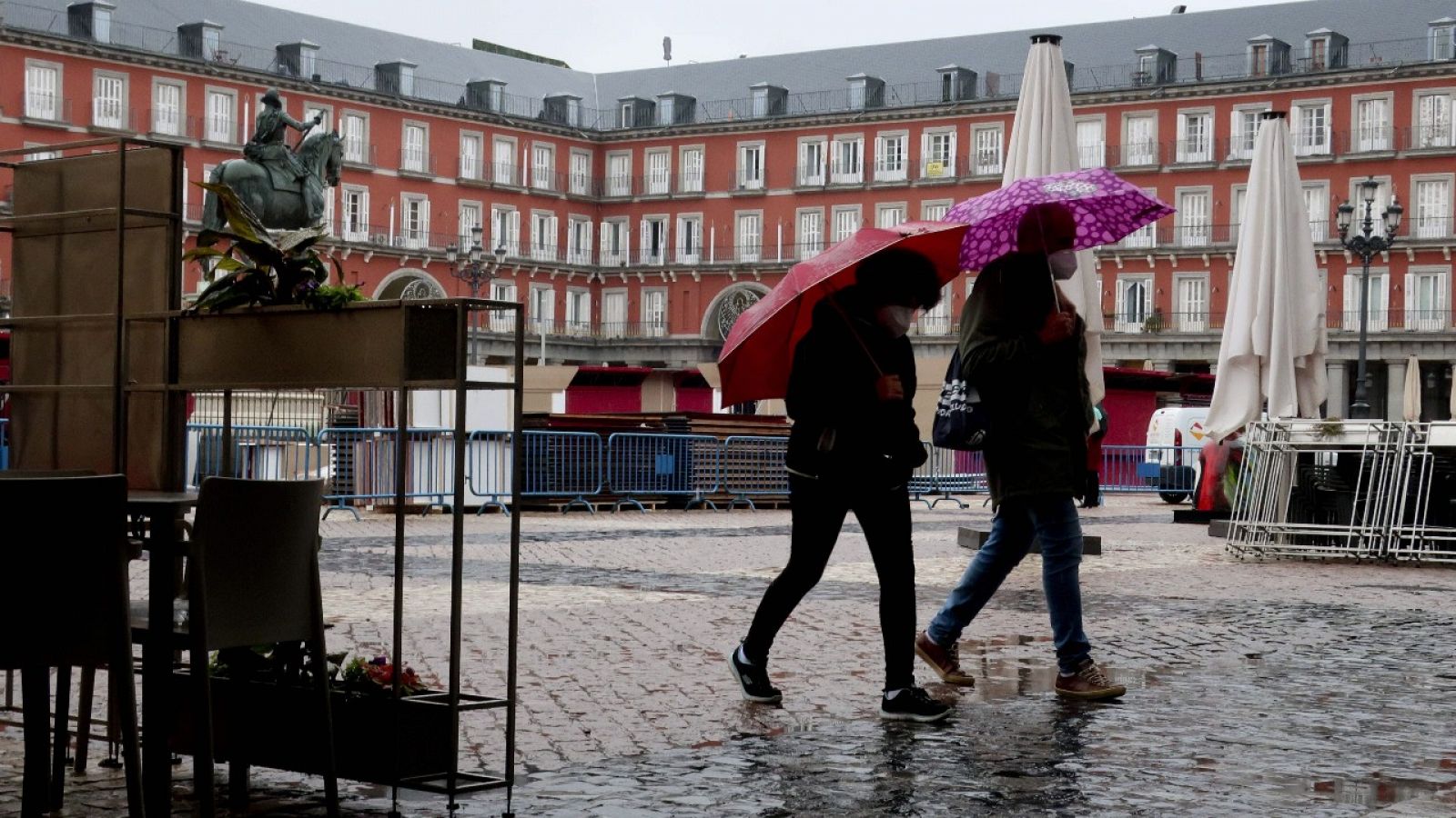 Dos personas caminan por la Plaza Mayor de Madrid, donde ya instalan el tradicional mercadillo navideño