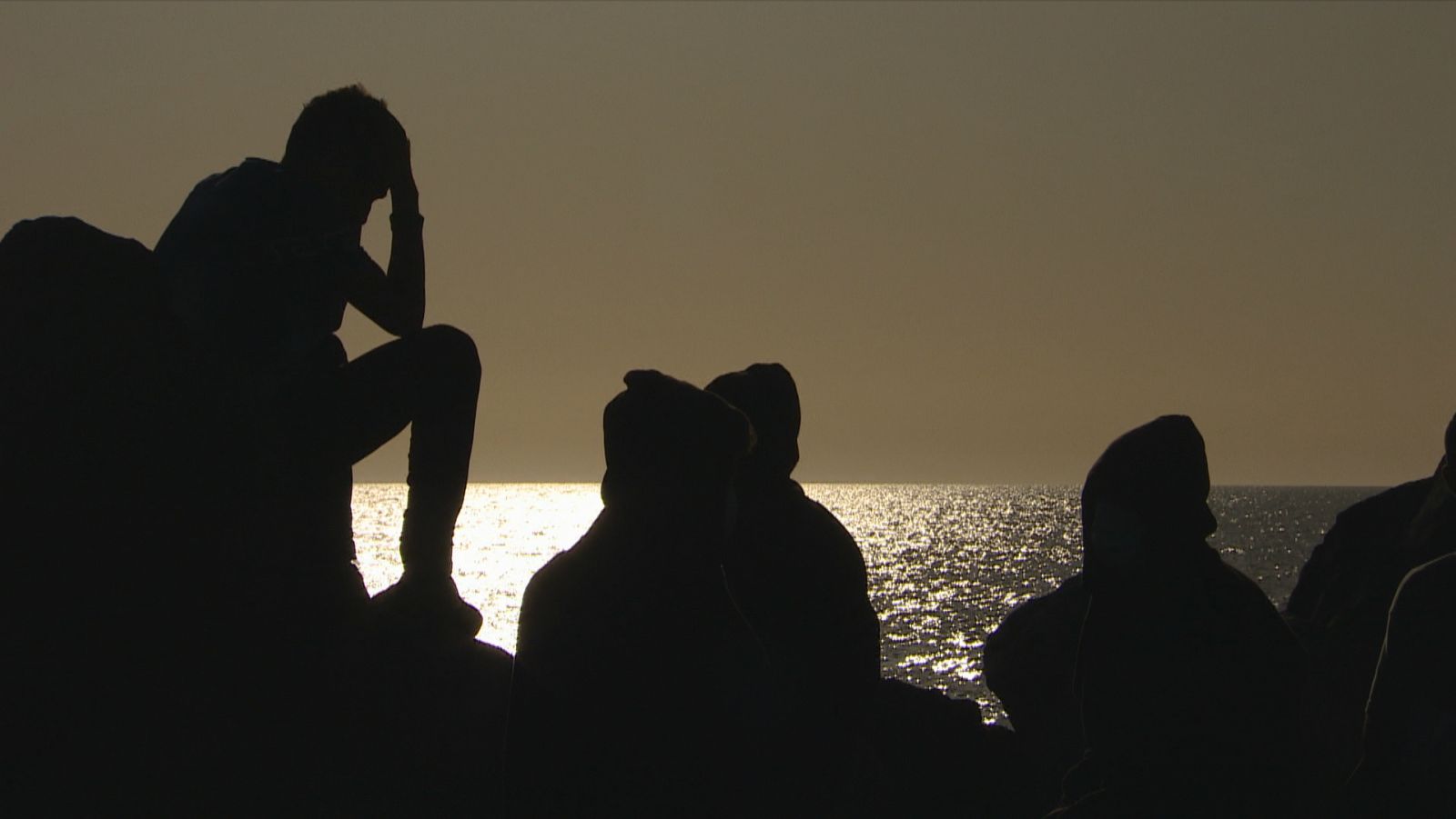 Varios migrantes esperan en el muelle de Arguineguín