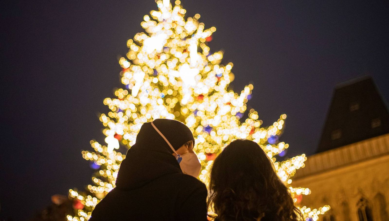 Una pareja ataviada con mascarillas sanitarias observan un árbol de Navidad