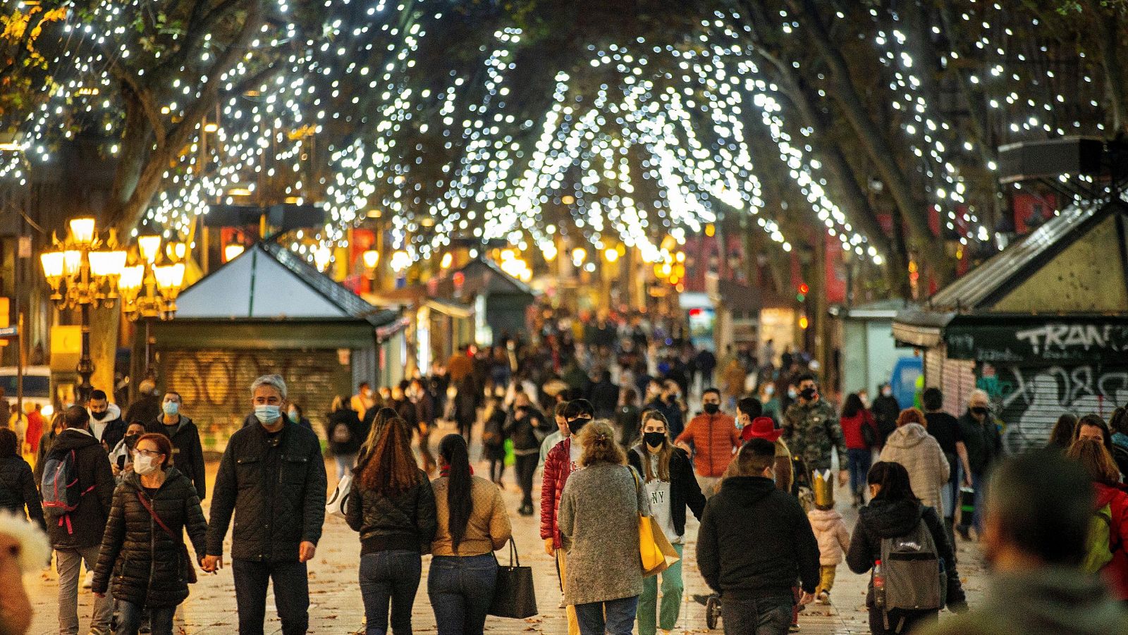 Varias personas pasean por las Ramblas de Barcelona con mascarilla bajo árboles adornados con luces de Navidad.