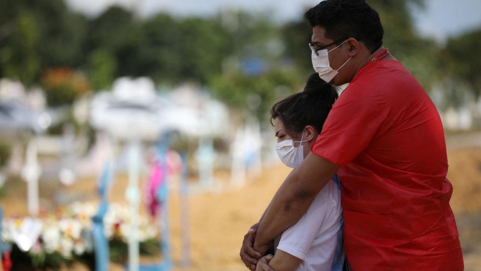 Dos personas con mascarilla durante el entierro de una víctima de la COVID-19 en un cementerio de Manaus, Brasil.