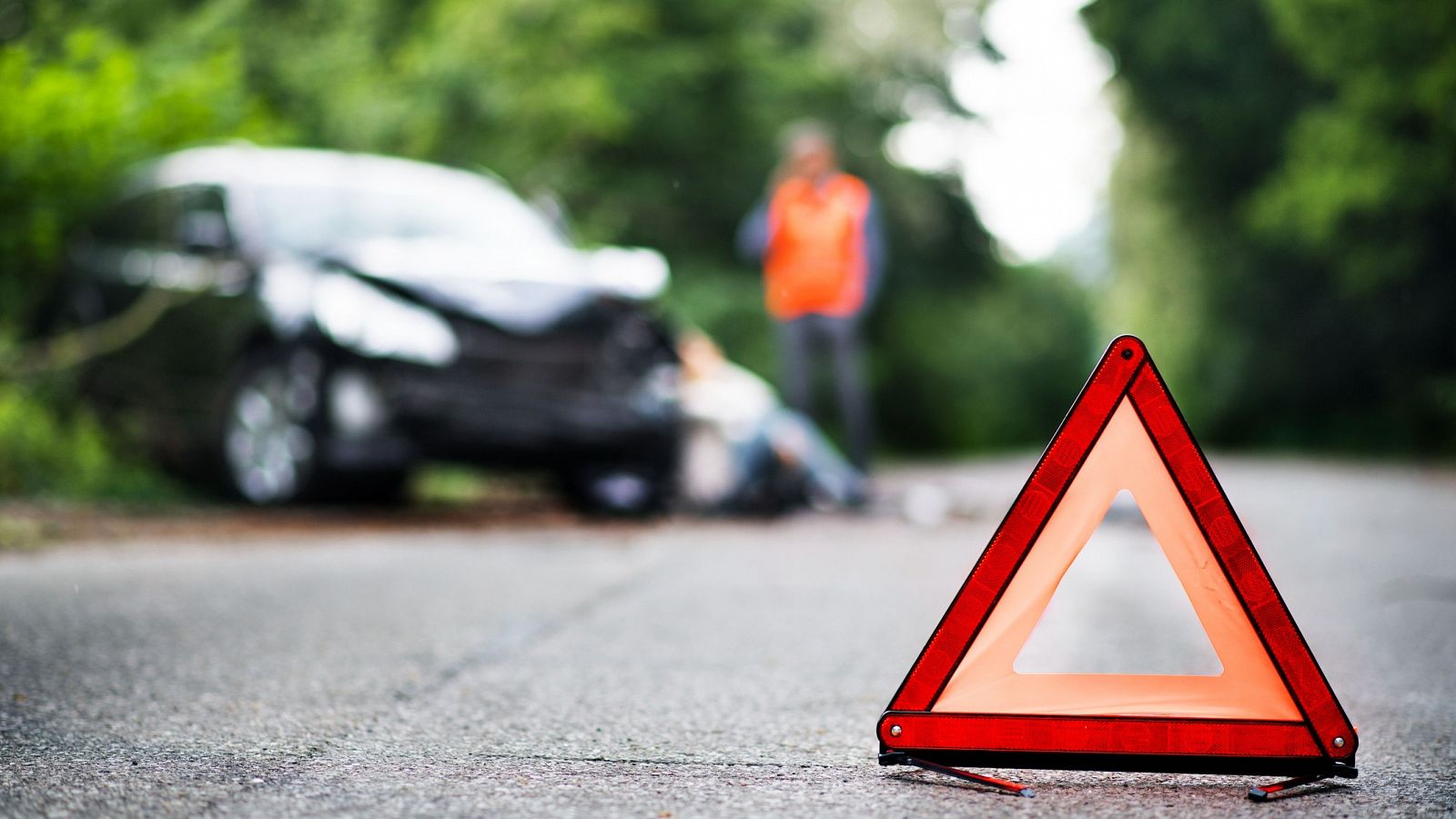 Primer plano de un triángulo de emergencia en una carretera frente a un vehículo accidentado.