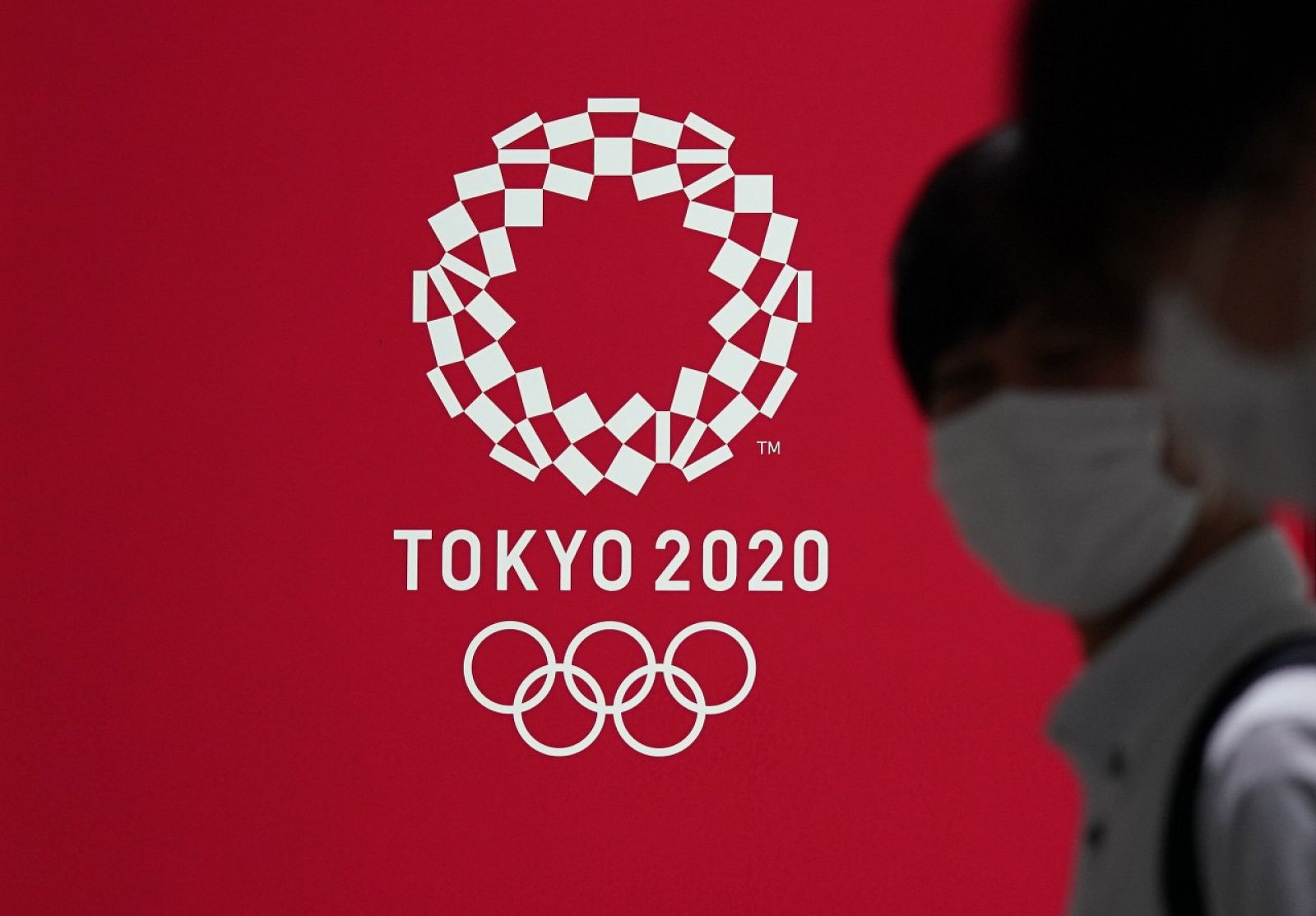Fotografía de archivo de dos personas con mascarilla pasando frente a un cartel con la imagen de los Juegos Olímpicos Tokio 2020 el 15 de julio de 2020 en la capital de Japón.