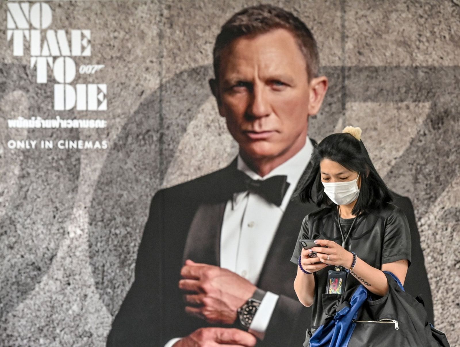 Una mujer con mascarilla pasando por delante de un cartel anunciando la nueva película de James Bond 'No Time to Die' en una calle de Bangkok, Tailandia.