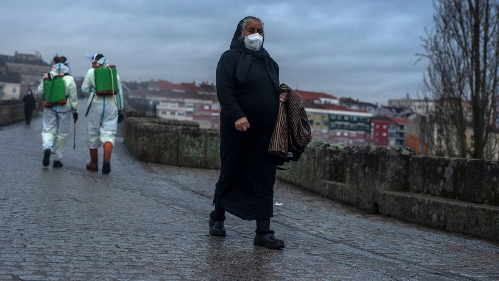 Una viandante cruza el Puente Romano de Ourense mientras empleados municipales lo desinfectan este martes. EFE/Brais Lorenzo