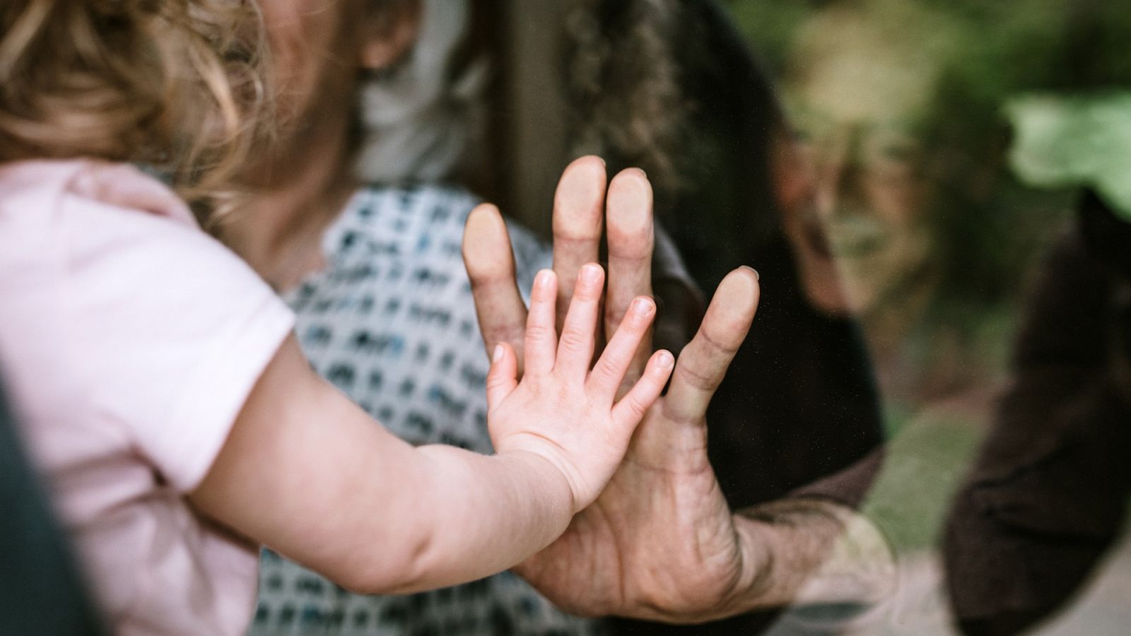 Una niña saluda a sus abuelos a través de un cristal.