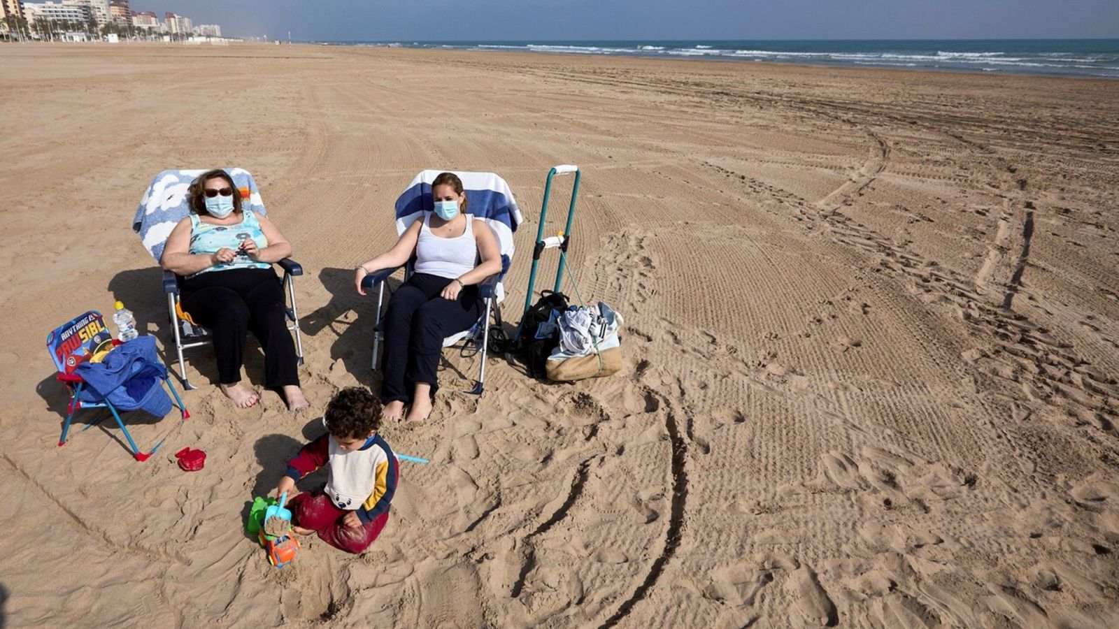 Varias personas toman el sol con mascarilla en la playa de Gandía (Valencia). EFE/ Natxo Frances