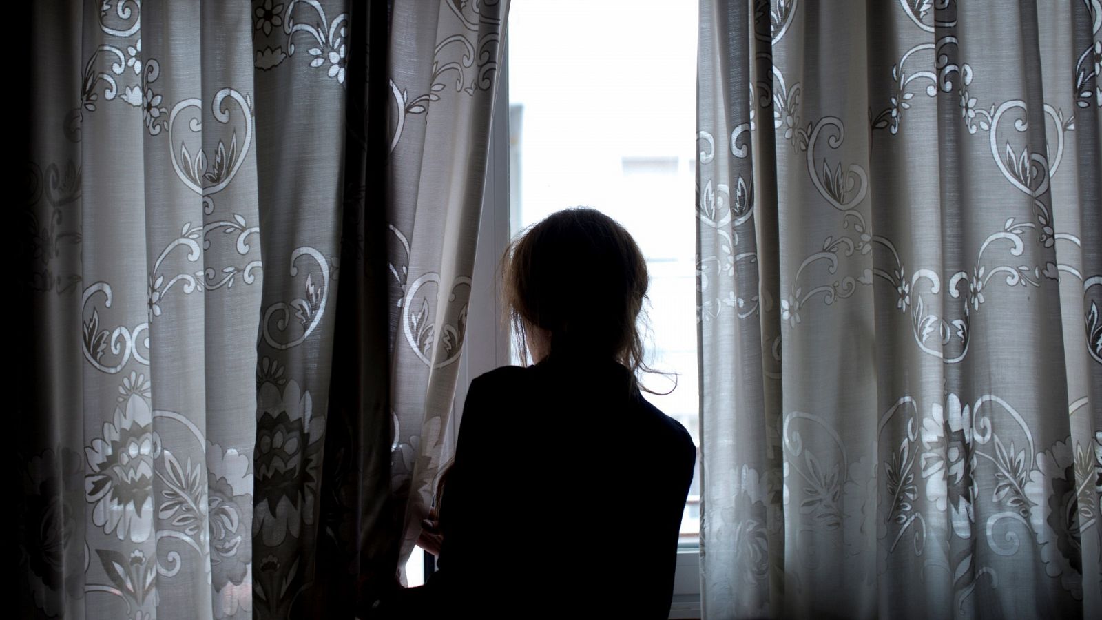 Una mujer observa a través de la ventana de su vivienda