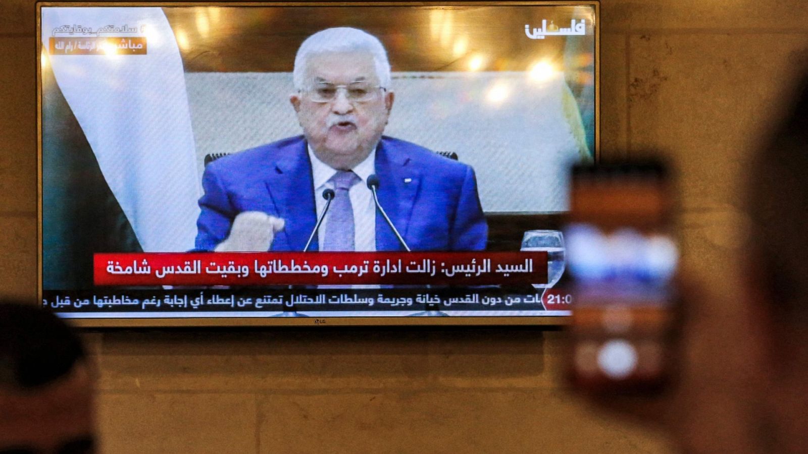 Un hombre haciendo una foto a una pantalla de televisión en la que se ve al presidente palestino, Mahmud Abás, dando un discurso el jueves 29 de abril de 2021.