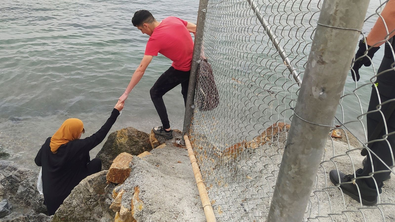 Dos inmigrantes escalan las rocas de uno de los espigones fronterizos de Ceuta este martes.