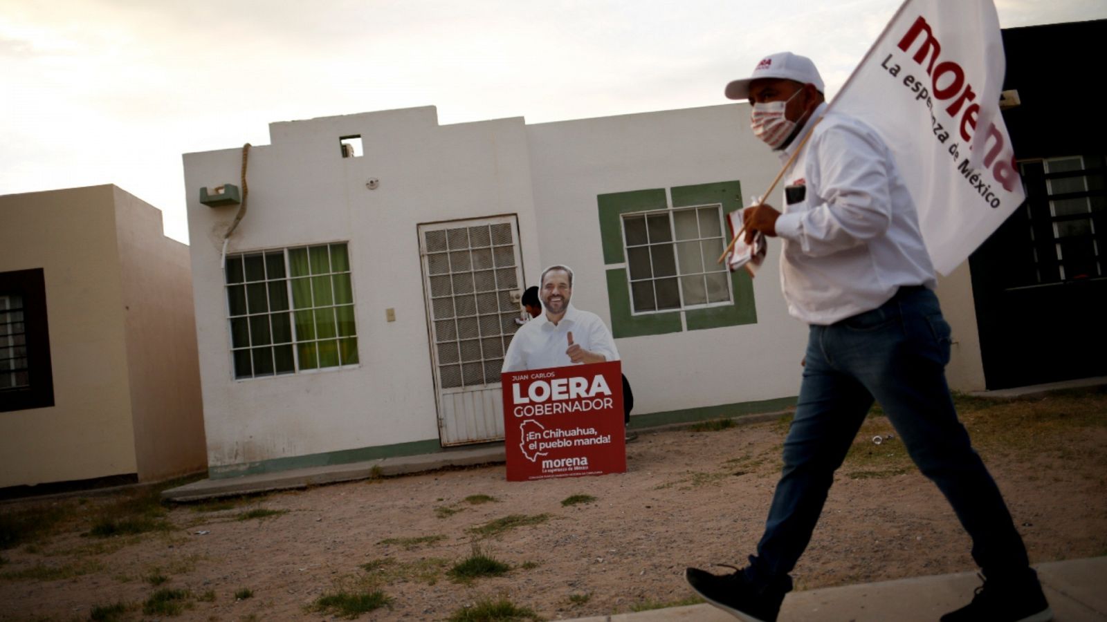 Un hombre sosteniendo una bandera electoral frente a un cartel de Juan Carlos Loera, candidato del partido Movimiento de Regeneración Nacional (MORENA) a gobernador en el estado de Chihuahua, México.