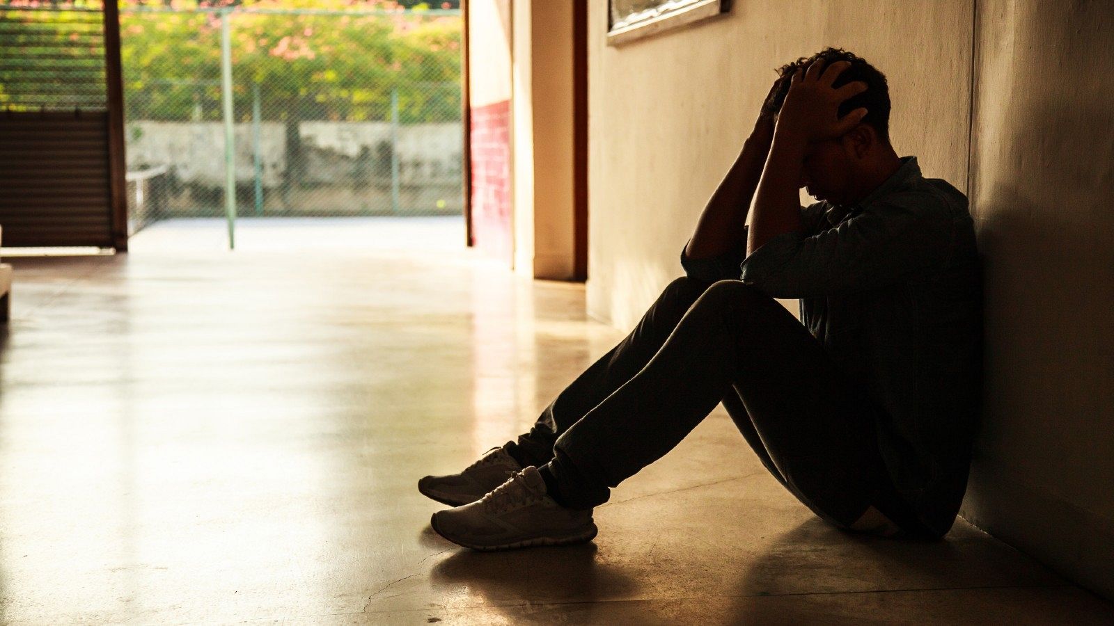 Un joven se sienta angustiado en los pasillos de un centro escolar.