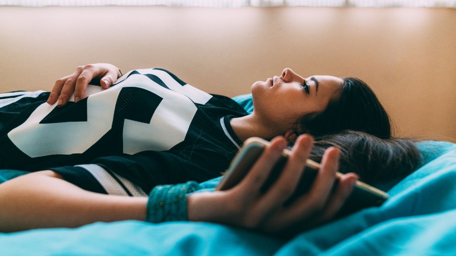 Una joven sostiene su teléfono mientras está echada en la cama