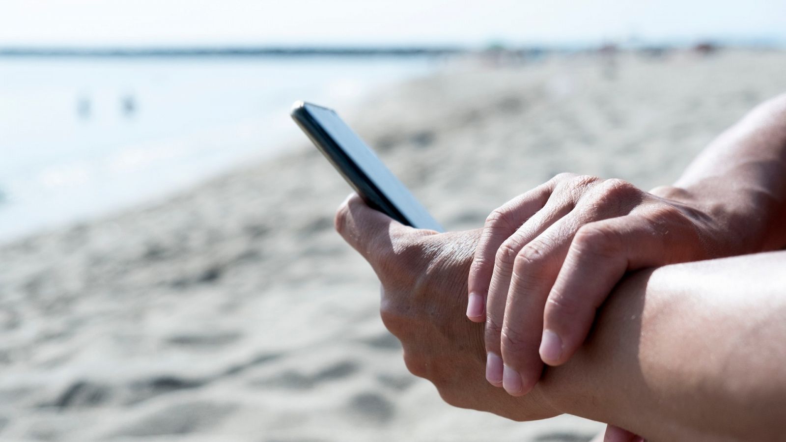 Una persona consulta su correo electrónico en el teléfono móvil desde una playa.
