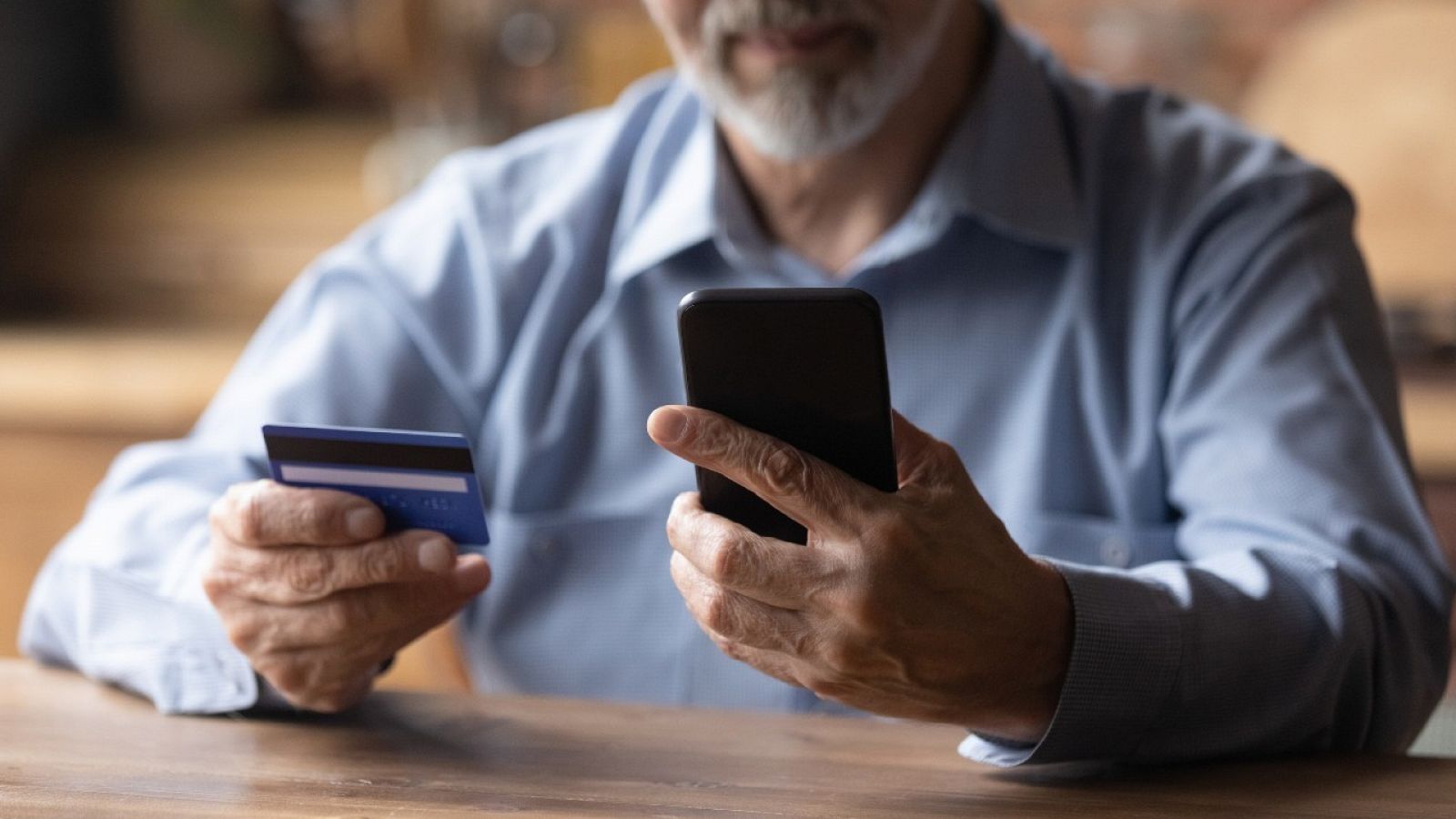 Un hombre utiliza su móvil mientras sostiene una tarjeta de crédito