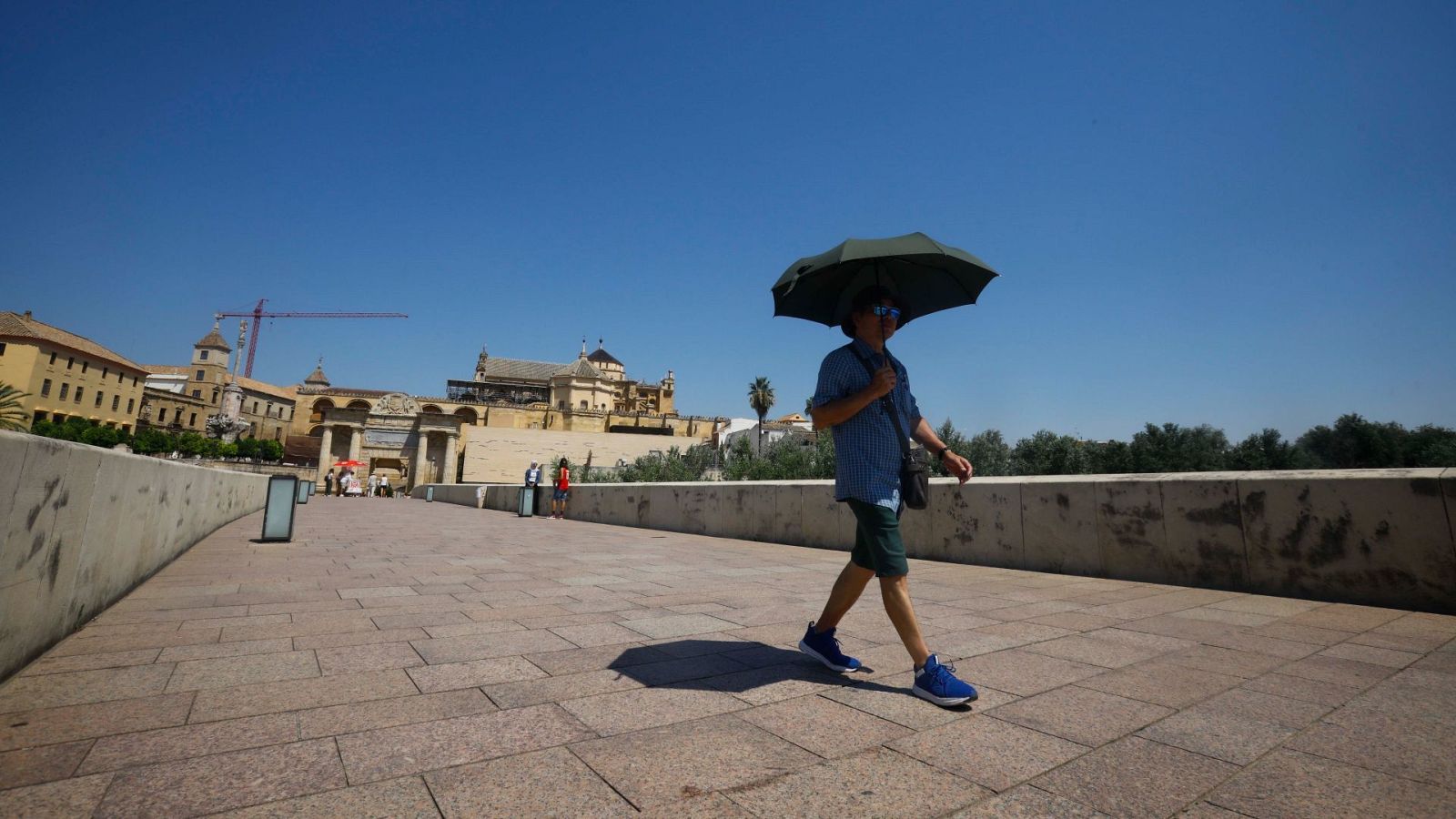 Un turista se resguarda del sol bajo un paraguas mientras camina por el Puente Romano de Córdoba