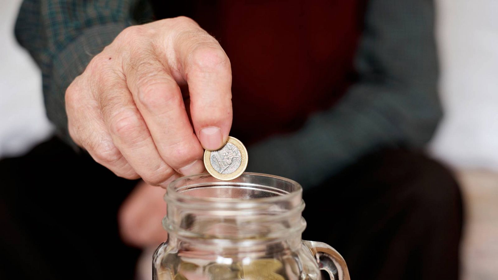 Imagen de un pensionista metiendo dinero en una hucha