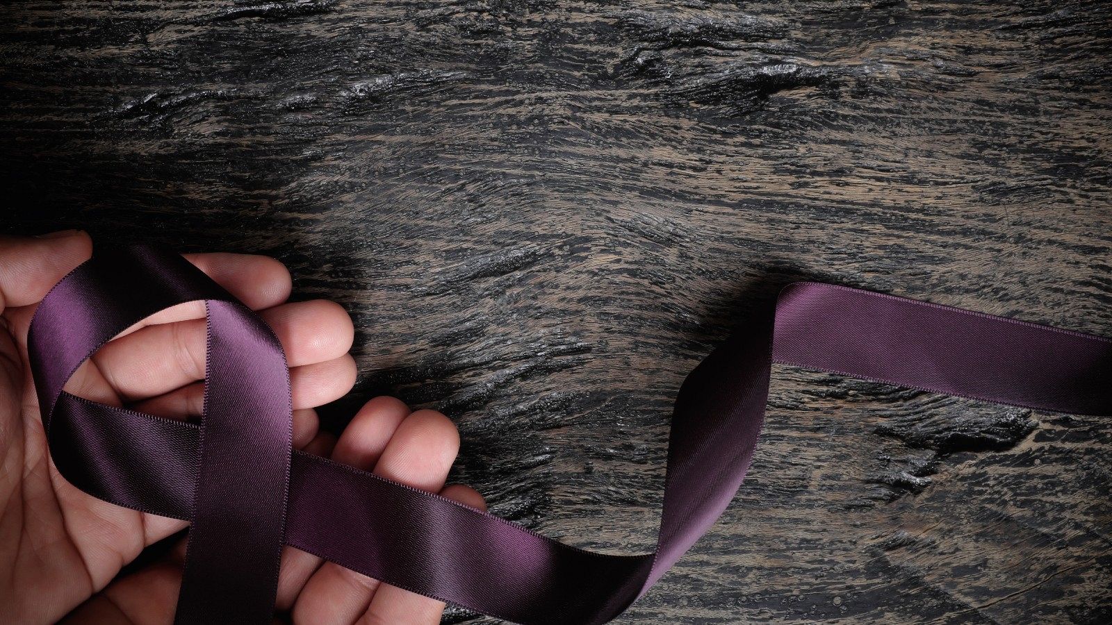 Dos manos sostienen un crespón violeta, símbolo contra la violencia de género