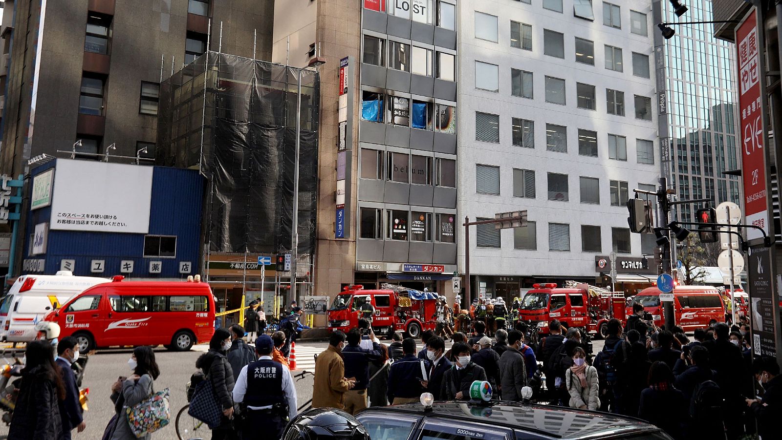 Coches de bomberos y policía, gente en la calle y el edificio que ha sufrido el incendio en plano general.