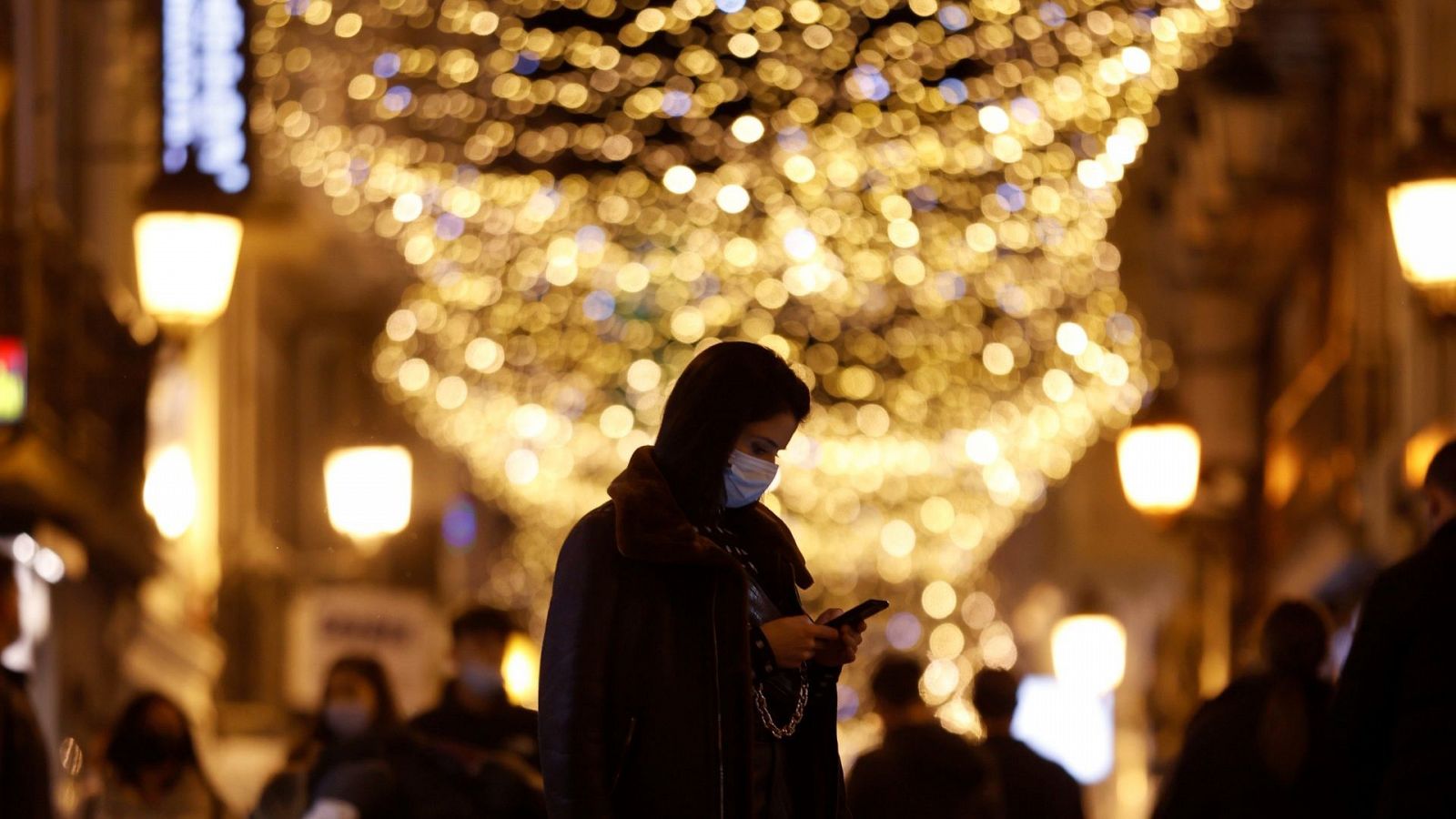 Una mujer observa su teléfono en una calle comercial por la noche