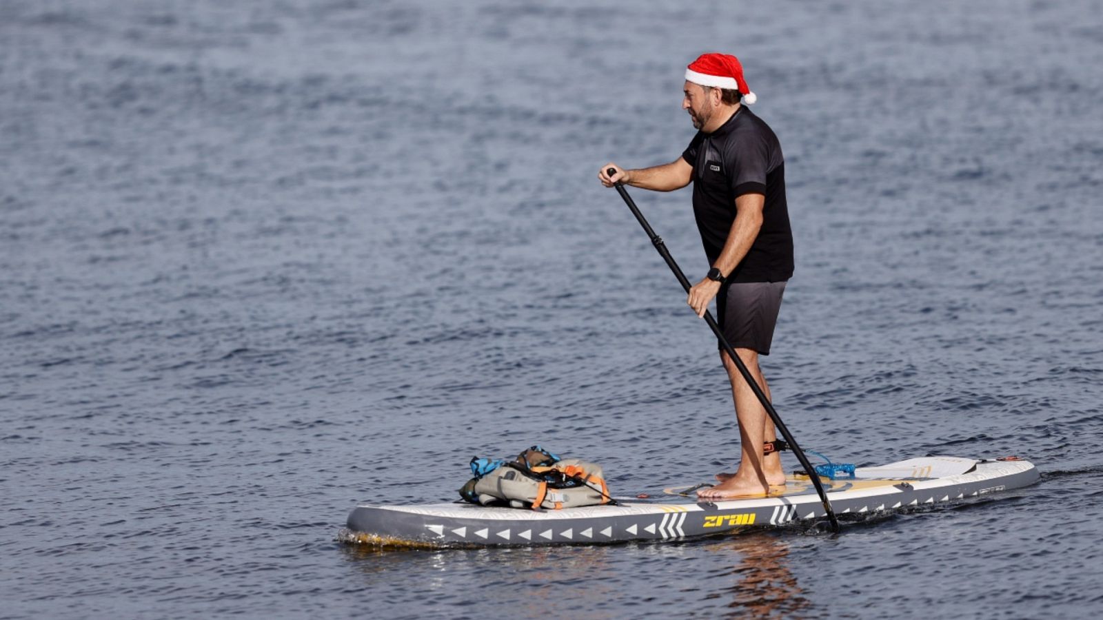 Una persona ataviada con un gorro de Papá Noel practicando paddle surf en las aguas de la playa de la Malvarrosa (Valencia).