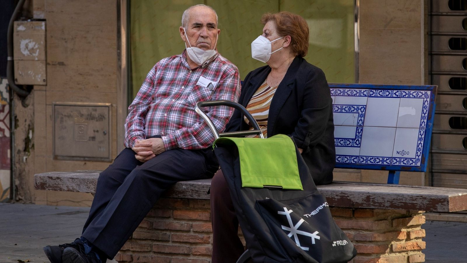 Una pareja está sentada en un banco de Sevilla con un carro de la compra
