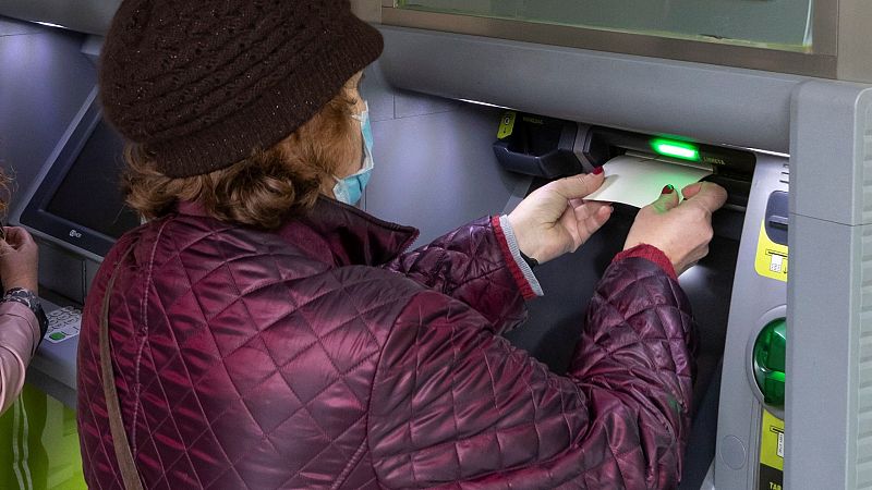 Una jubilada usa su libreta de ahorros en un cajero