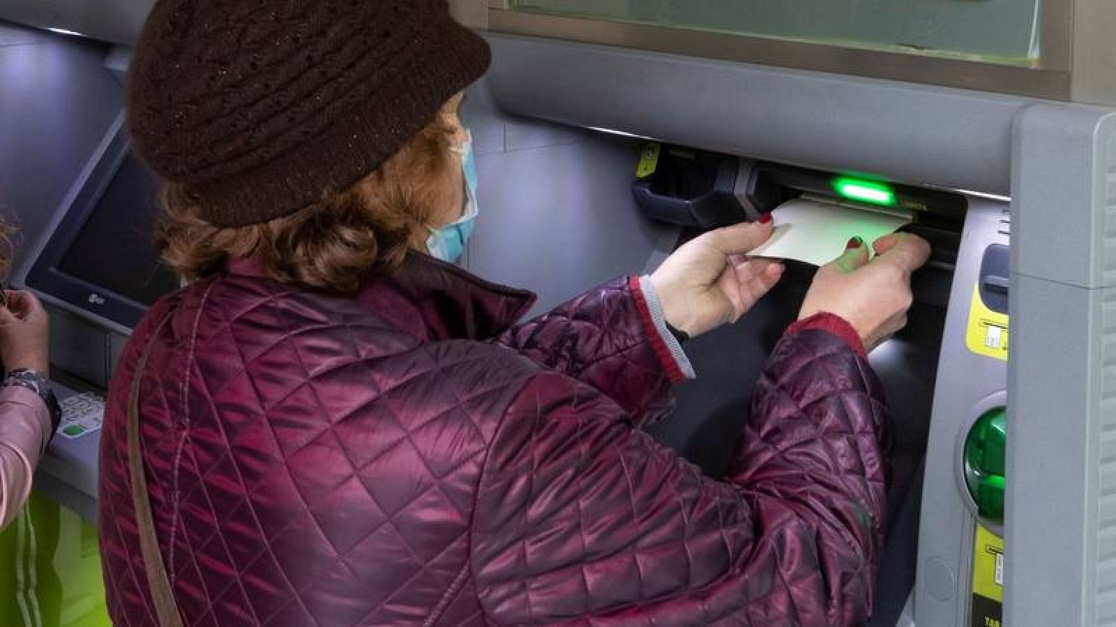 Una jubilada usa su libreta de ahorros en un cajero