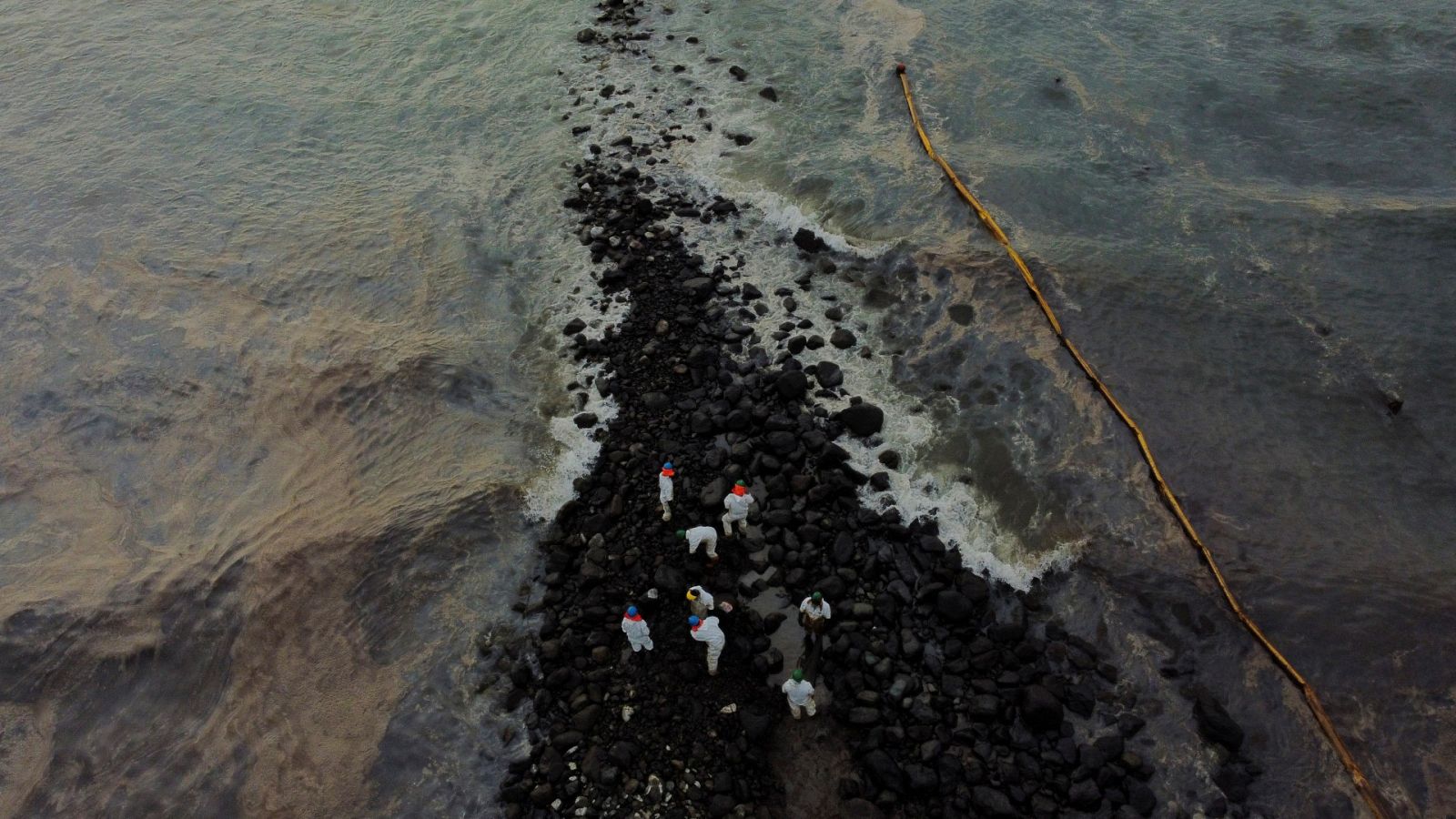 Trabajadores limpian la playa cercana a la refinería La Pampilla de Repsol