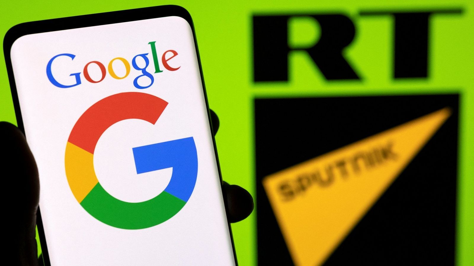El logo de Google visto en la pantalla de un teléfono frente a los símbolos de los canales rusos RT y Sputnik