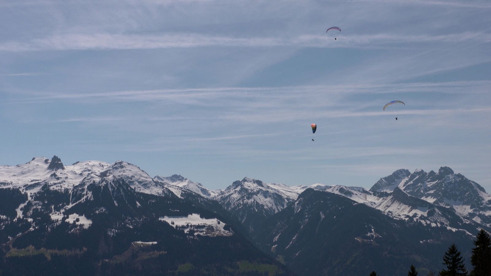 Paisatge de muntanyes nevades amb tres parapents al cel