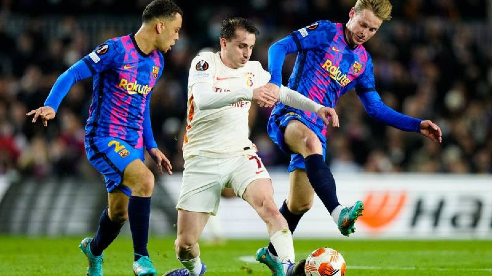 El delantero del Galatasaray Kerem Akturkoglu (c) pelea un balón con Sergiño Dest (i) y Frenkie De Jong. 