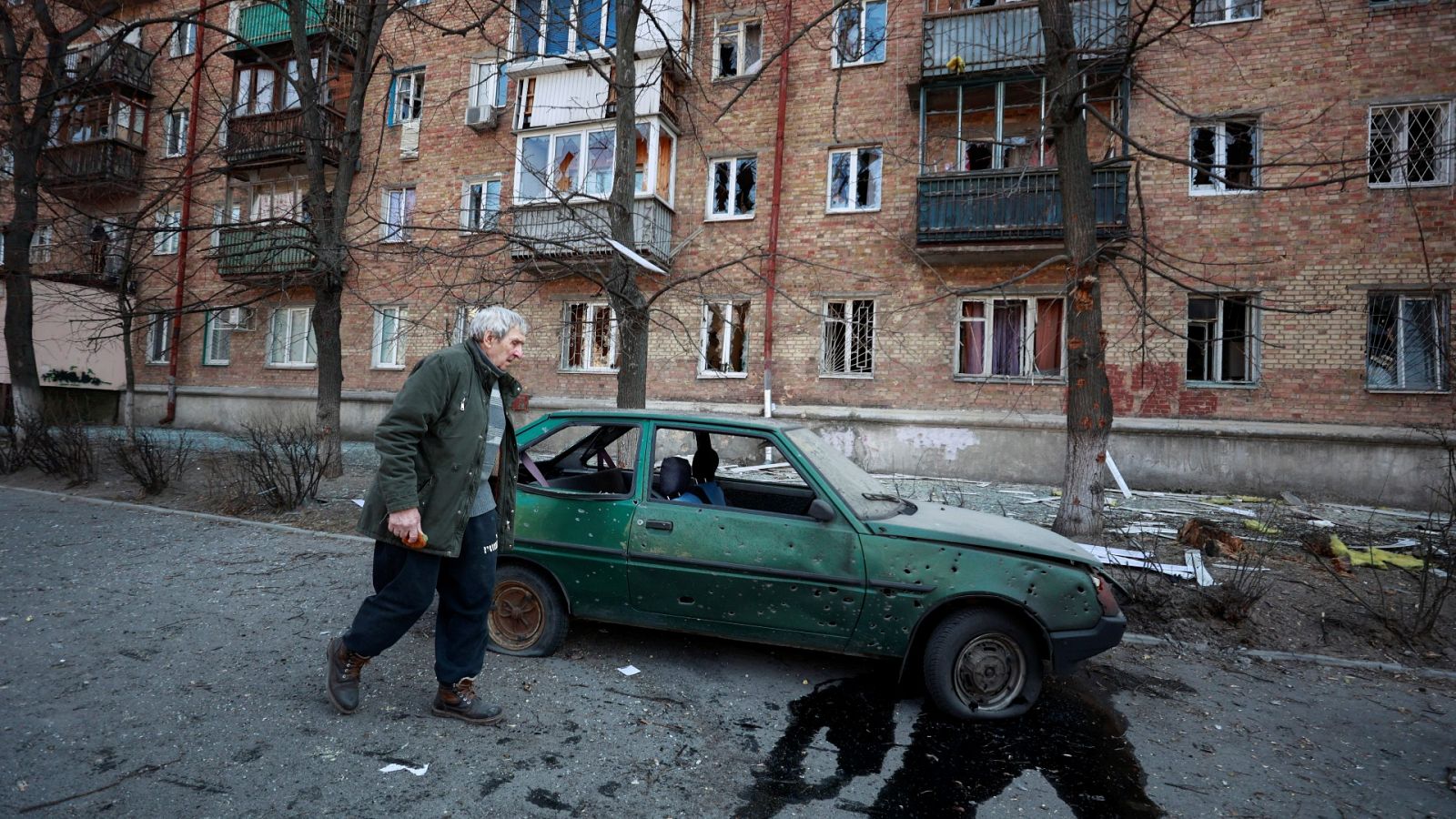 Un hombre junto a un vehículo y un edificio dañado en Kiev, Ucrania