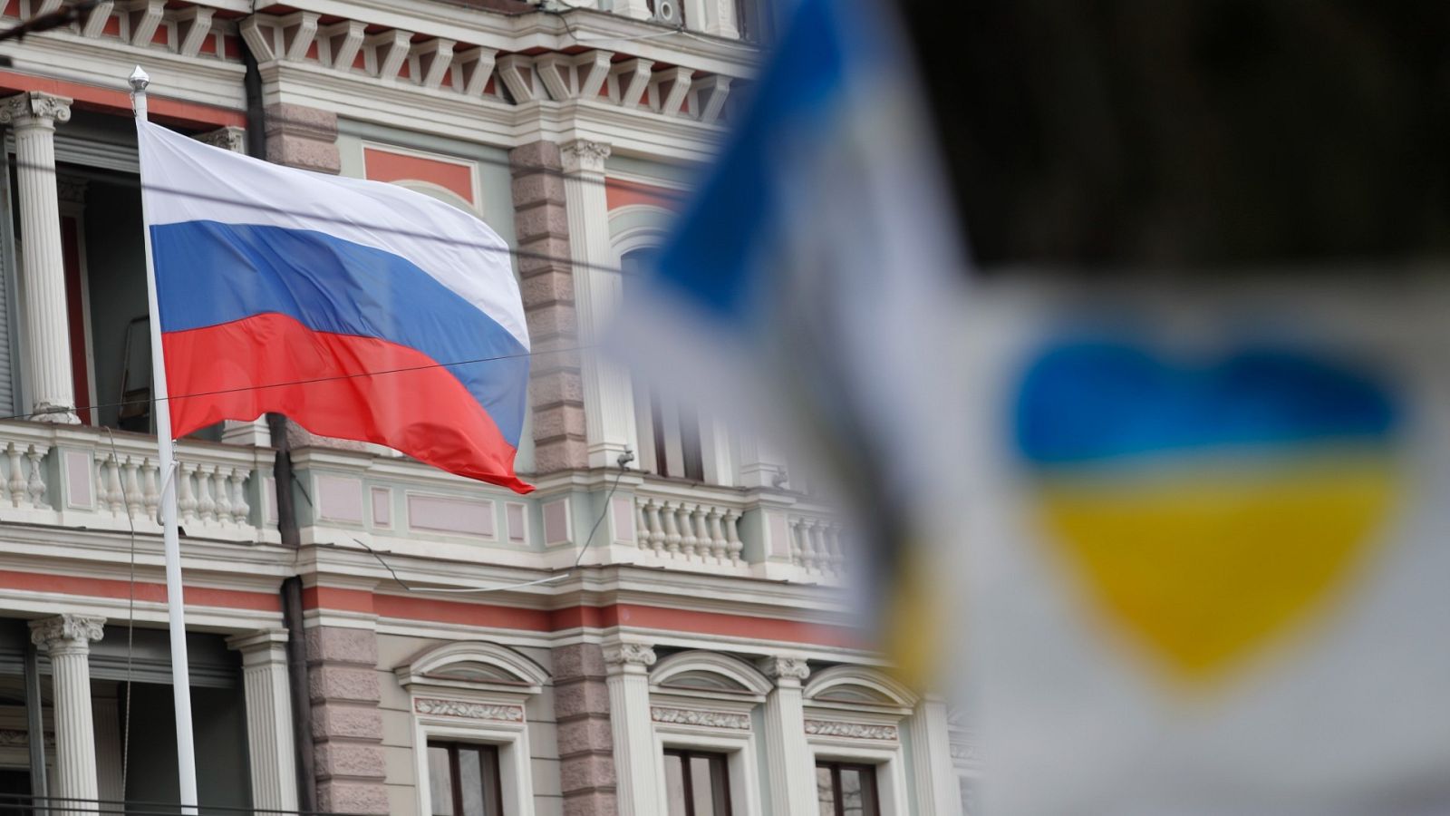 La bandera rusa ondea en la fachada de la embajada de Rusia en Letonia, con carteles en apoyo a Ucrania enfrente. 