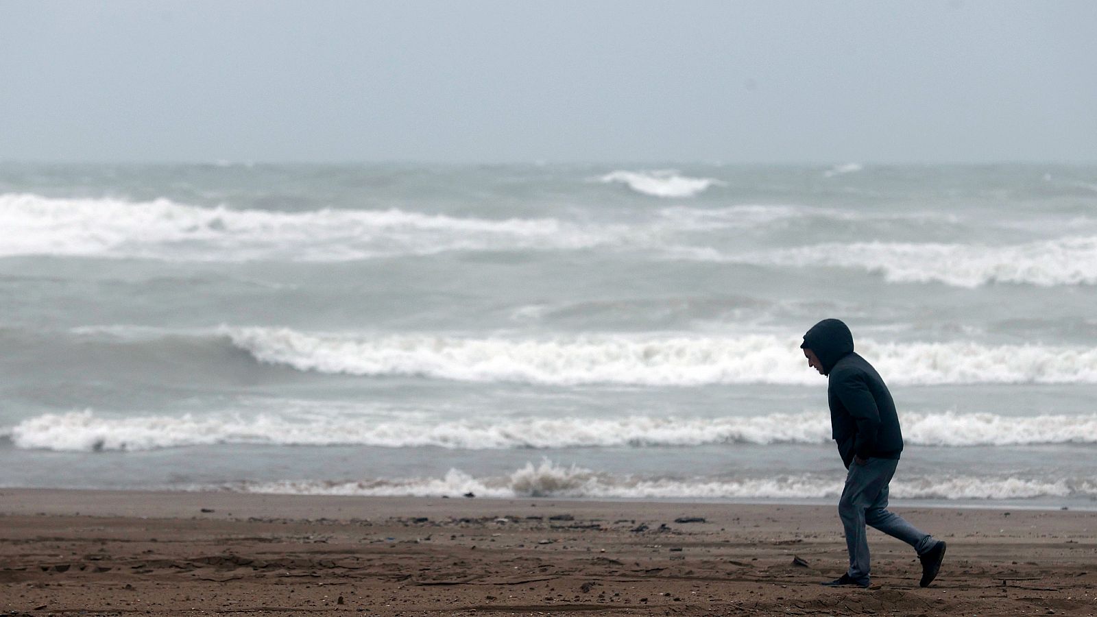 Un hombre camina por la playa ante un mar cubierto por las olas.