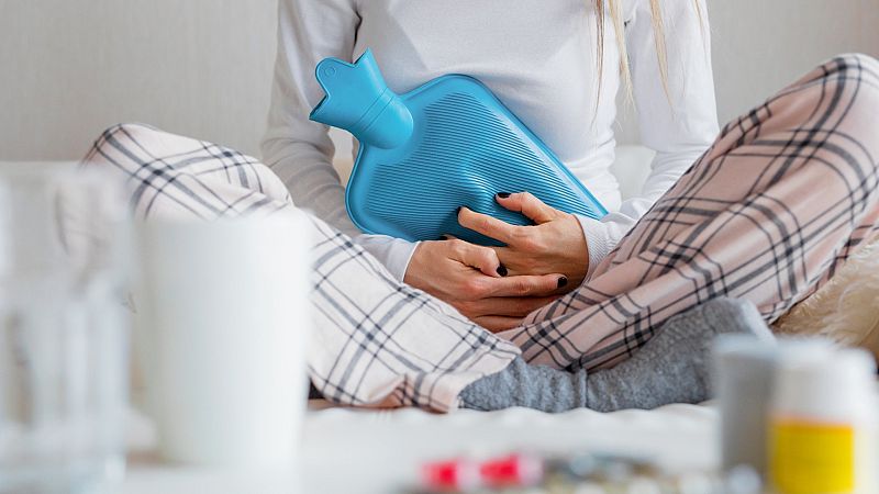 Una mujer aguanta el dolor menstrual con antiinflamatorios y una bolsa de calor, en una imagen de archivo