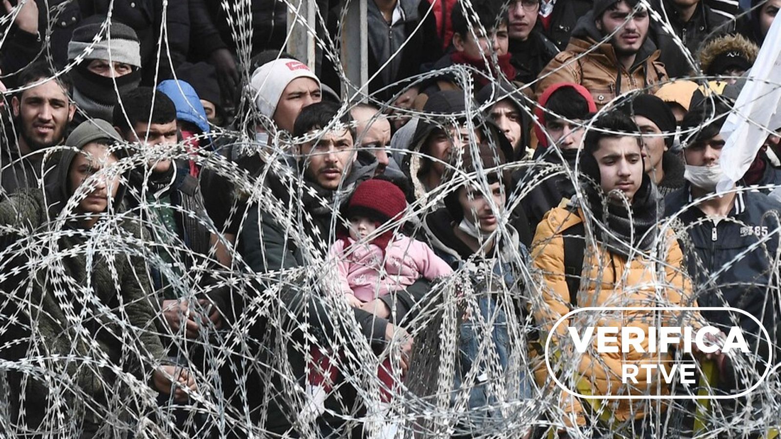 Imagen de migrantes esperando tras una verja en la frontera de Turquía con Grecia, con el sello blanco de VerificaRTVE