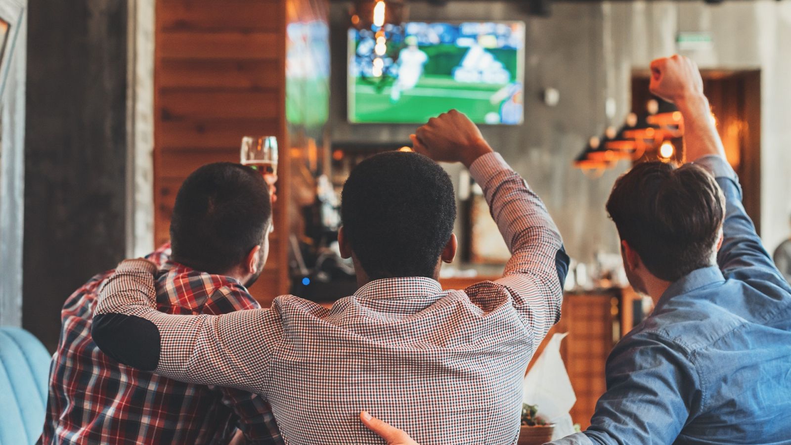 Tres hombres viendo un partido de fútbol en un bar